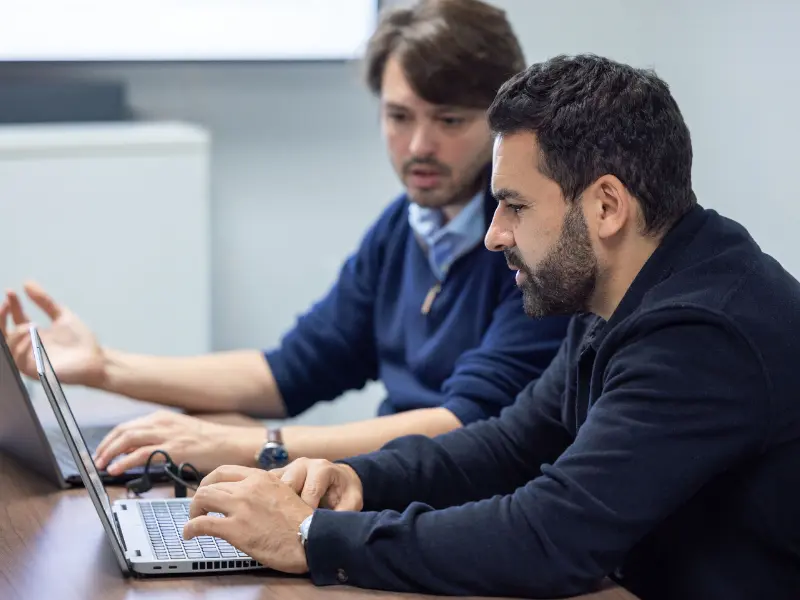 Dos expertos en tecnología colaboran en portátiles durante una revisión de due diligence técnica