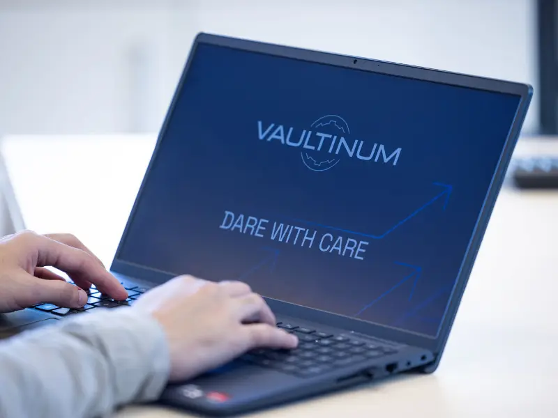 Personne travaillant sur un ordinateur portable affichant le logo Vaultinum et le slogan "Dare with care"