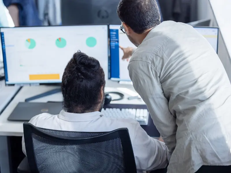 Two experts analyzing data on dual monitors, collaborating on technology performance reports.